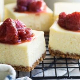 Cheesecake bars on a cooling rack topped with strawberry topping.