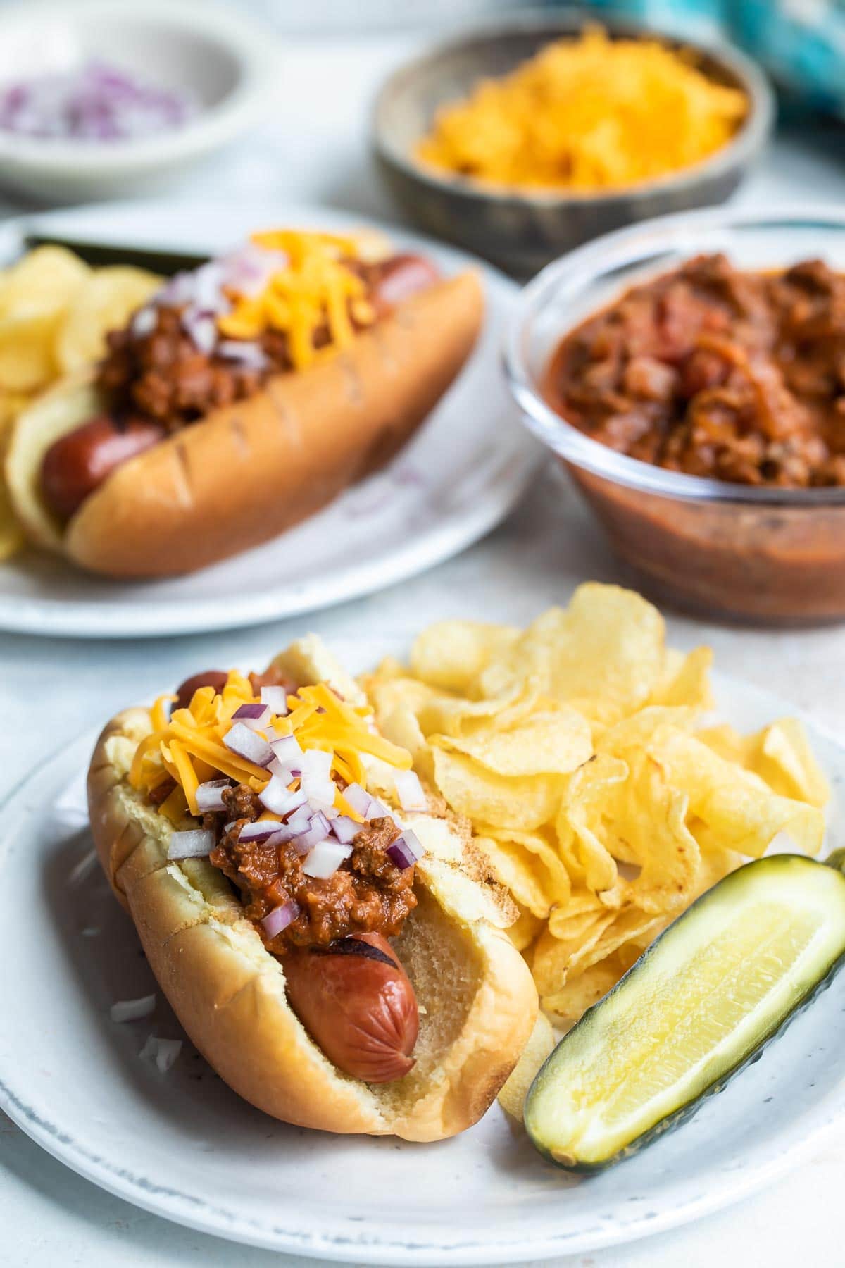 A chili dog on a plate with a pickle and chips.
