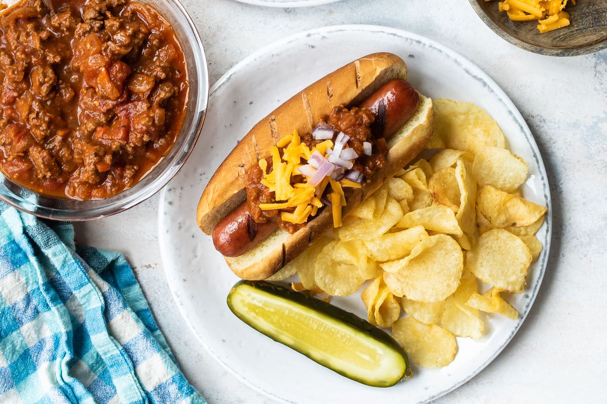A chili dog on a plate with a pickle and chips.