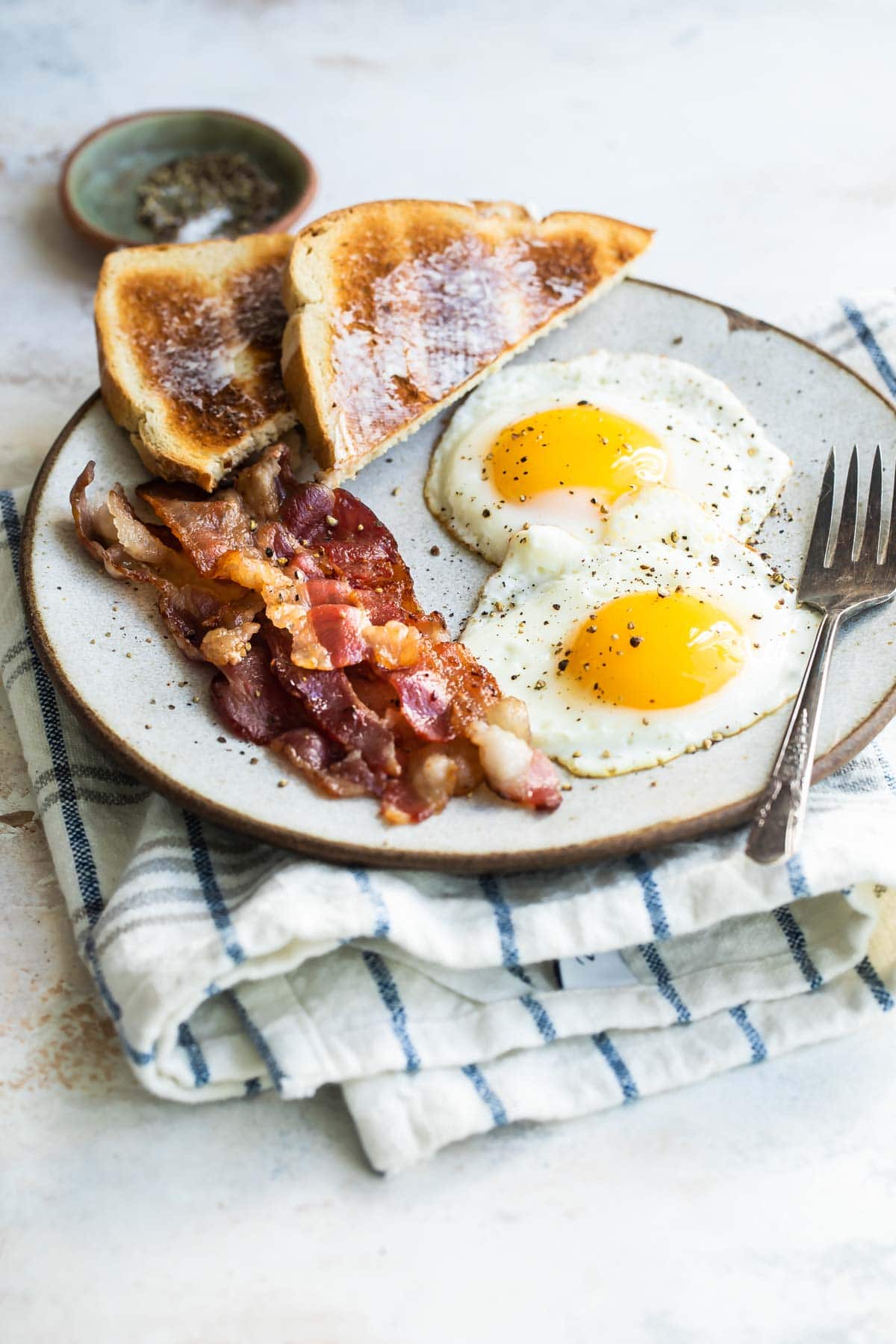 Sunny side up eggs on a plate with bacon and toast.