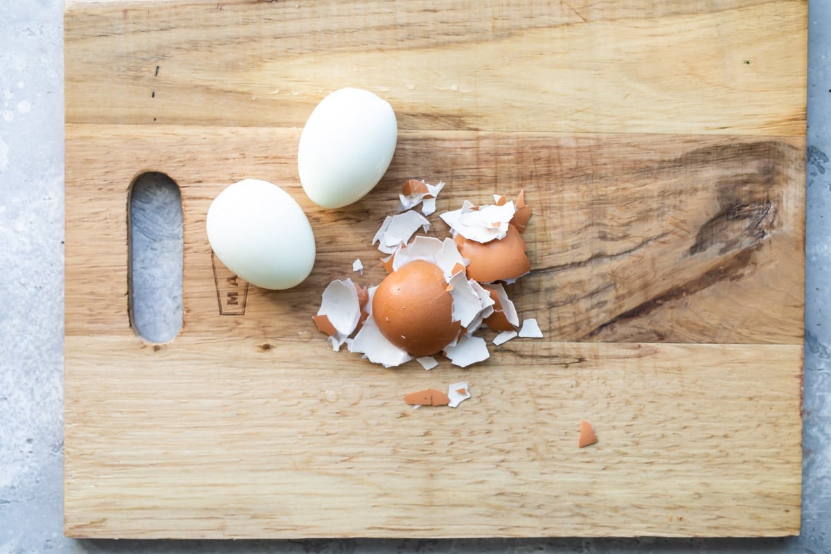 Two hard-boiled eggs peeled on a cutting board.