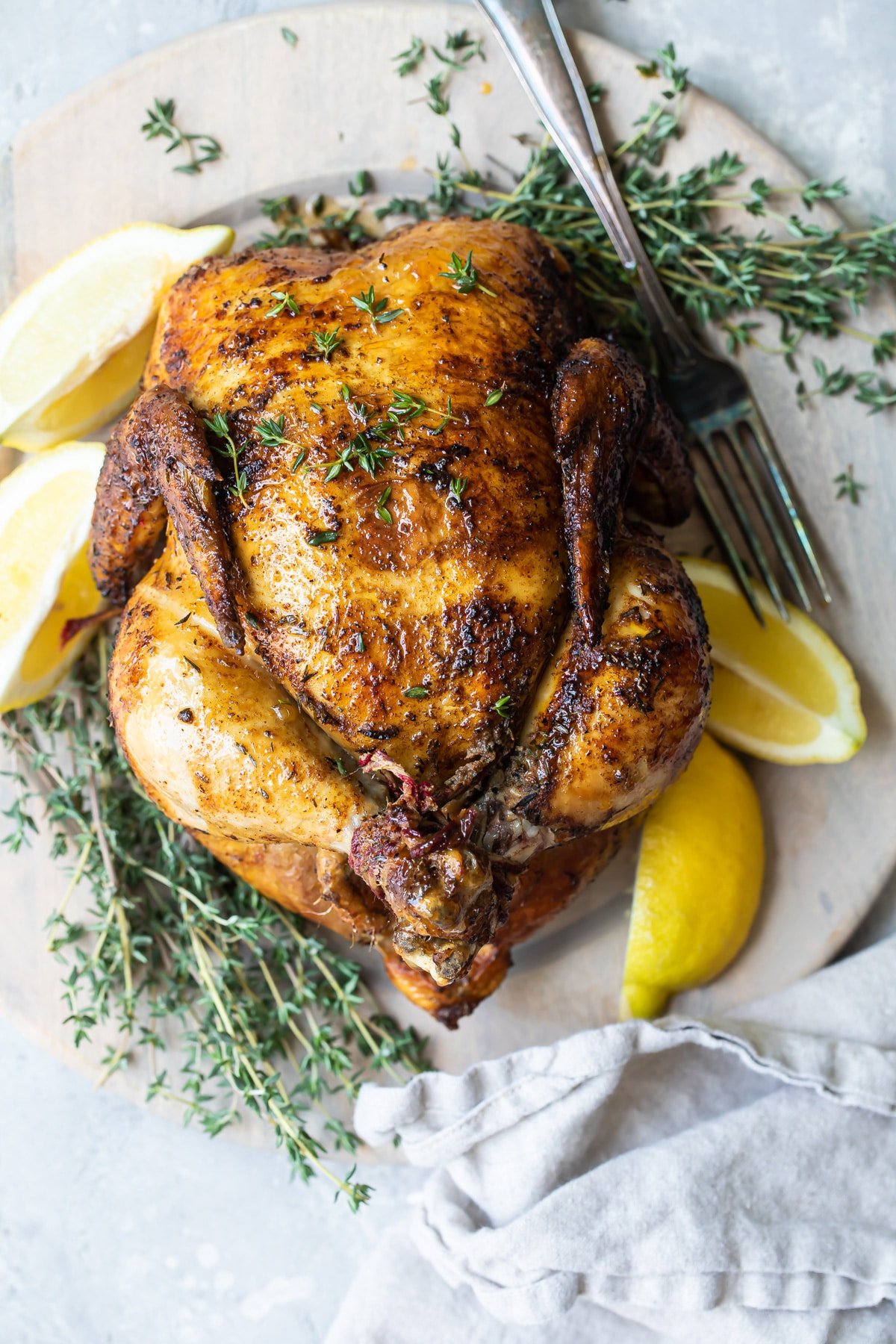 A rotisserie chicken on a white plate with slices of lemon.