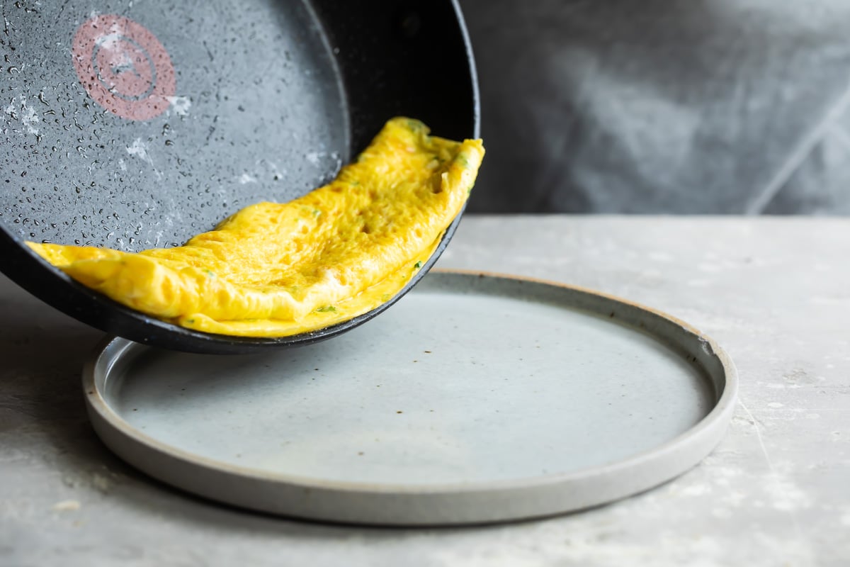 An omelet on a gray plate with a side of fruit.