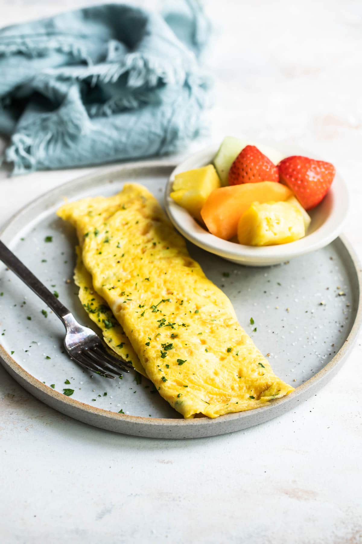 An omelet on a gray plate with a side of fruit.
