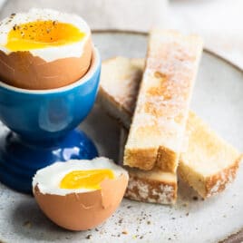 A soft boiled egg in a blue egg cup with toast sticks next to it.