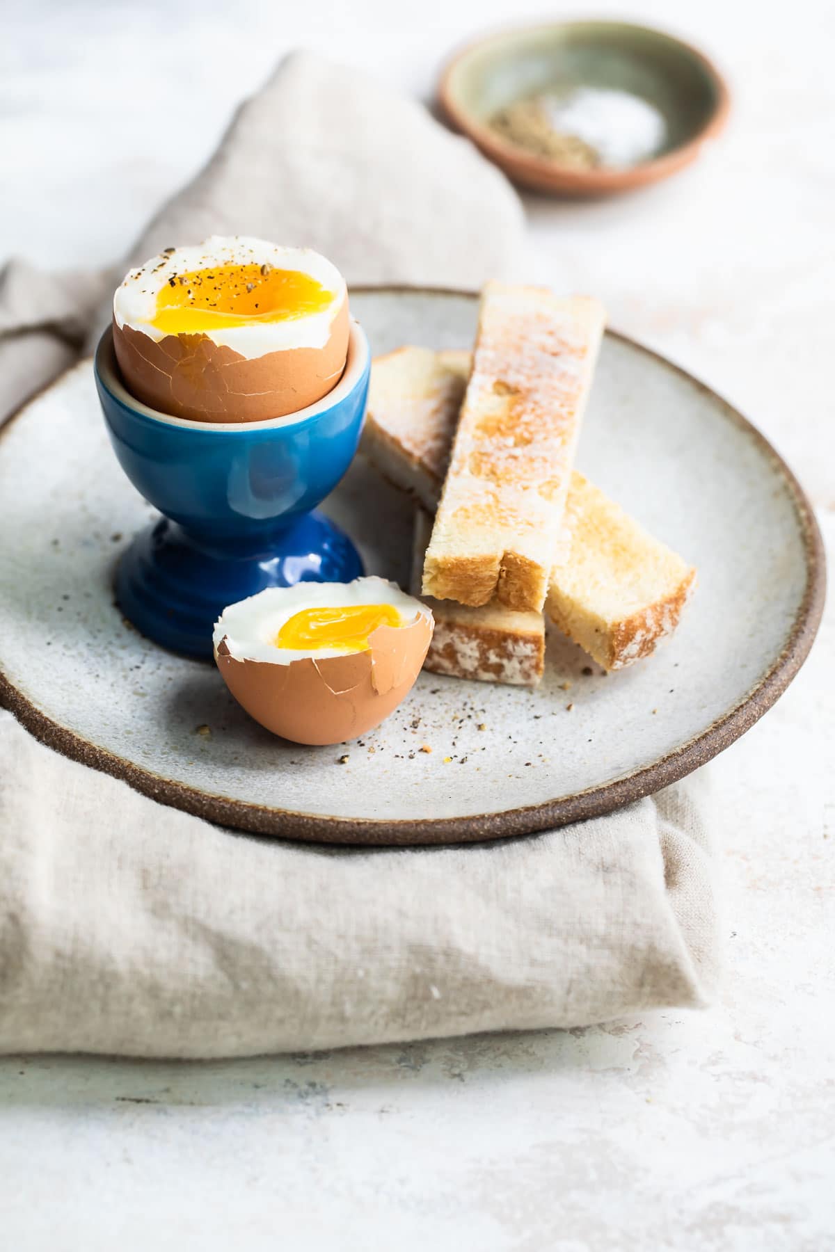 A soft boiled egg in a blue egg cup with toast sticks next to it.