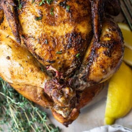 A rotisserie chicken on a white plate with slices of lemon.