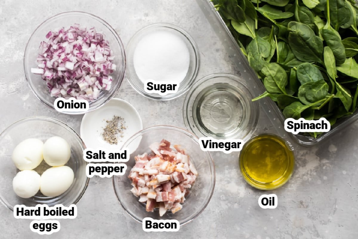 Spinach salad with bacon dressing ingredients in various bowls.
