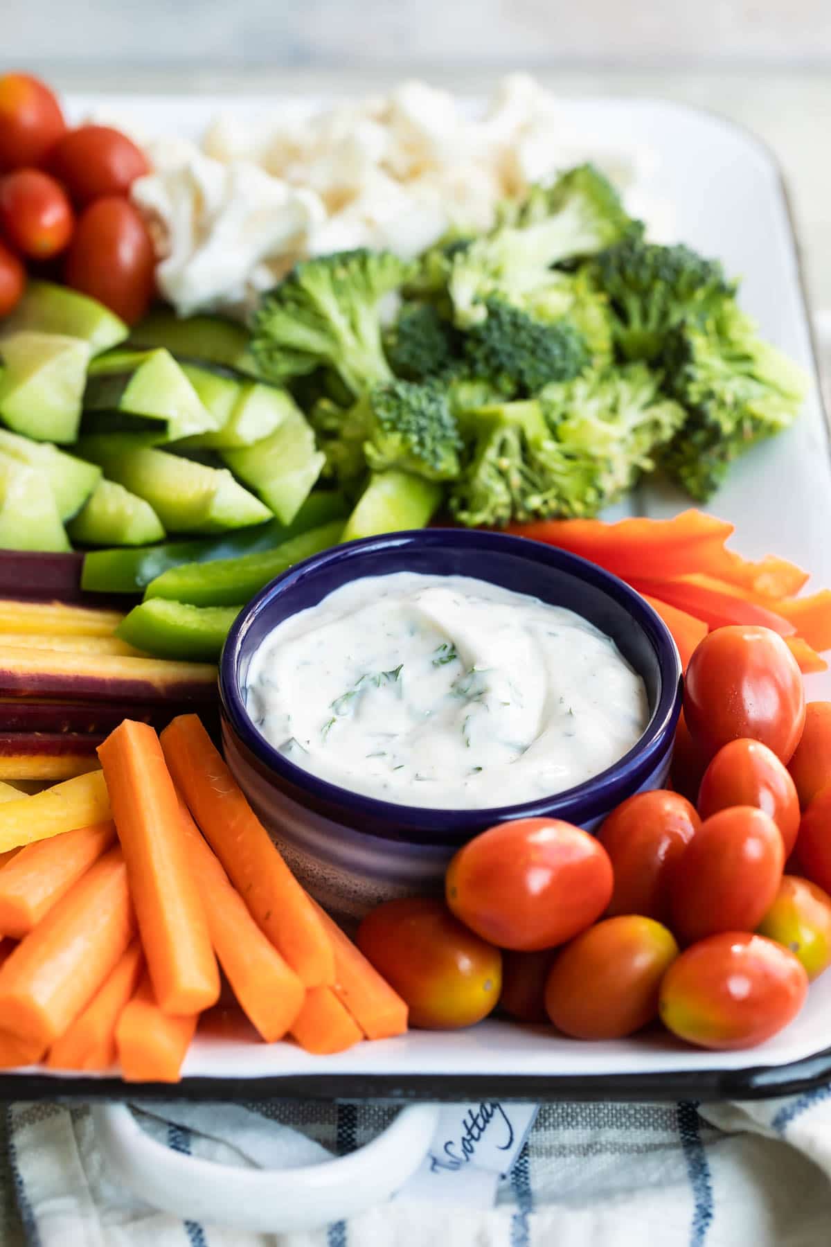 Veggie dip in a navy bowl bowl on a platter surrounded by vegetables.