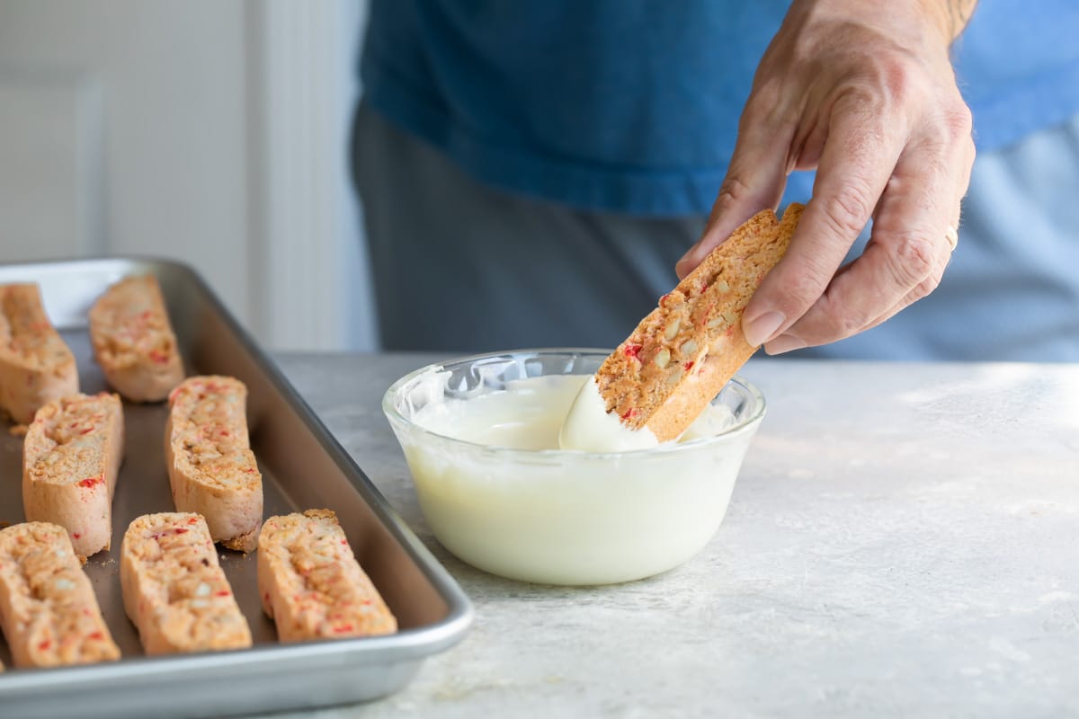 Cherry almond biscotti being dunked in melted white chocolate.