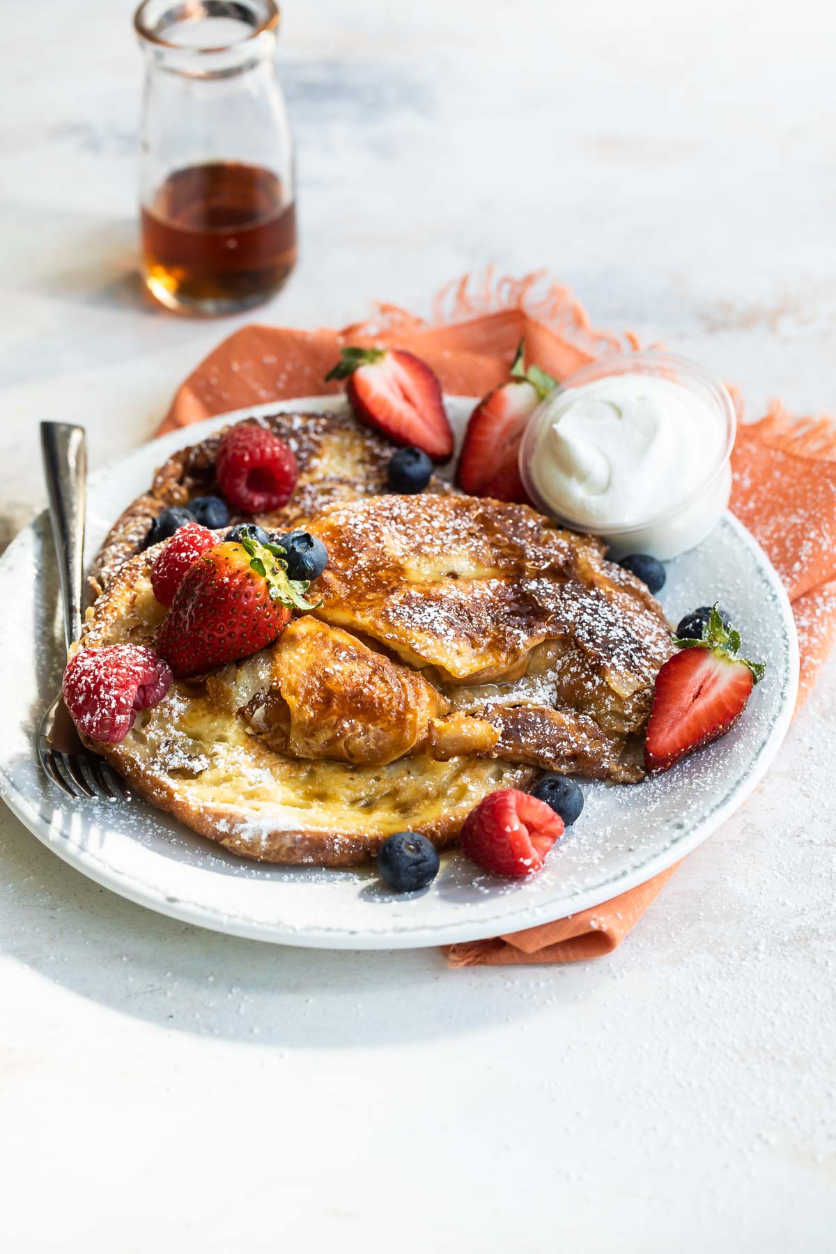 Croissant French toast on a white plate with fruit and whipped cream.