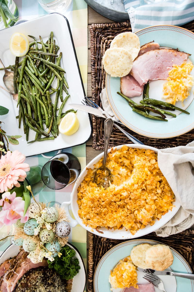 A table set for Easter with baked ham, scalloped potatoes, roasted green beans, and homemade biscuits.