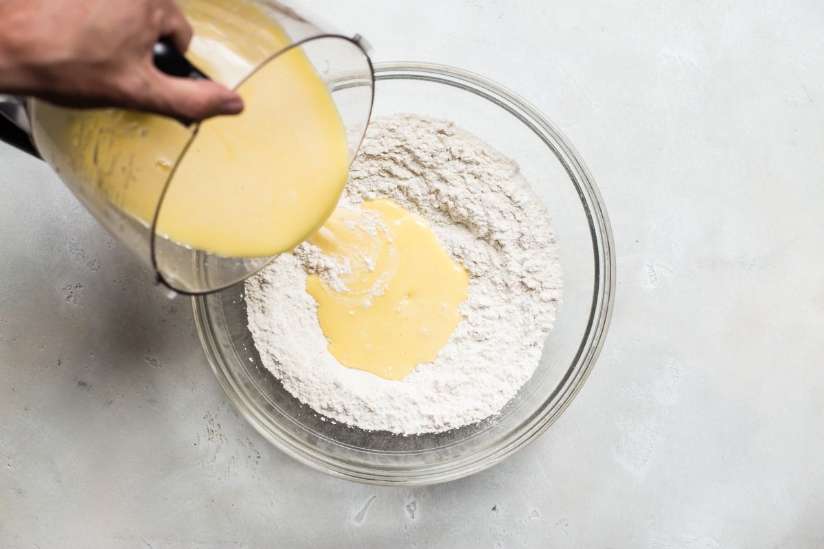 An overhead shot of egg mixture being poured onto dry ingredients in a clear bowl.