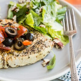 A piece of grilled swordfish on a plate with olive topping and green salad.