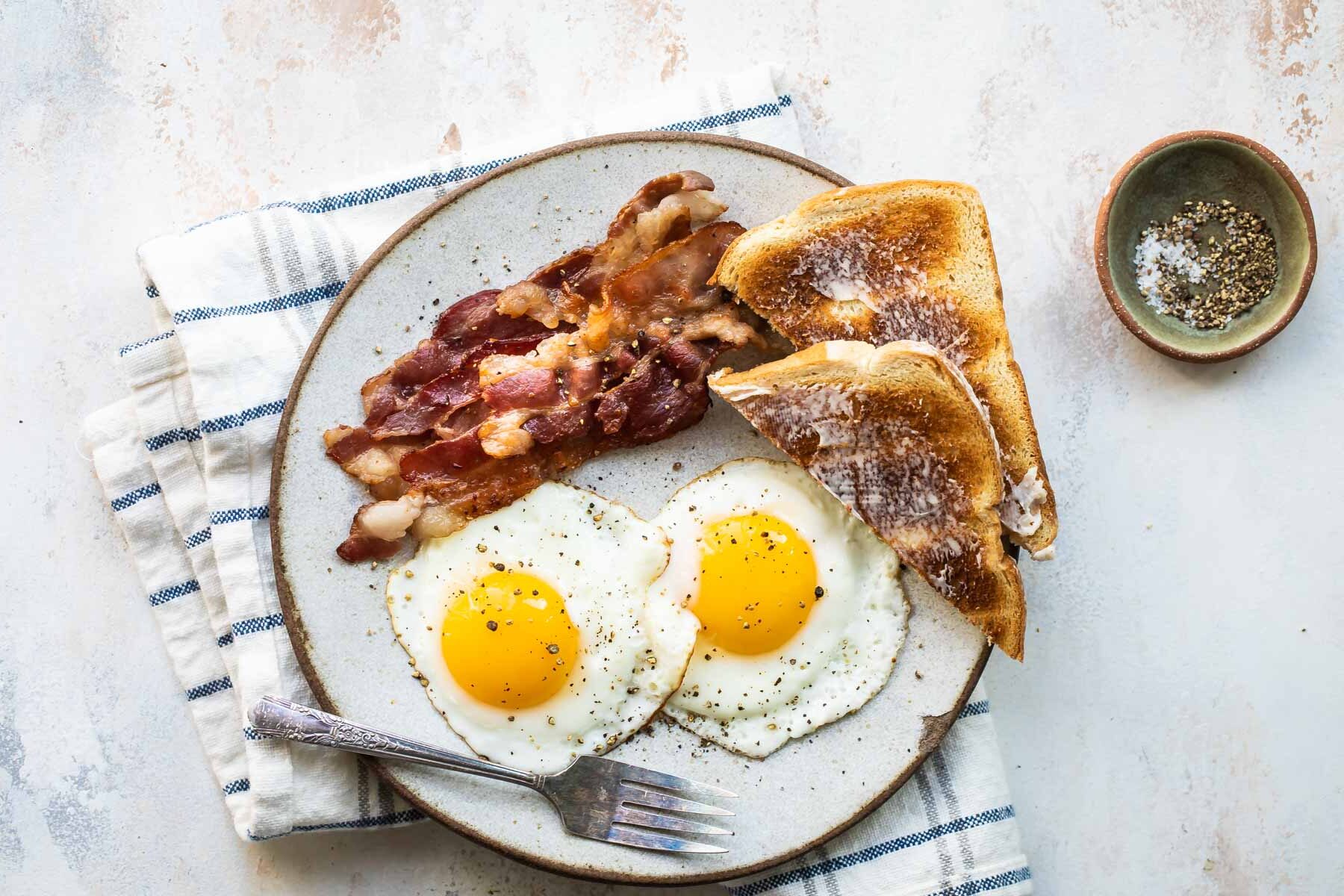 Sunny side up eggs on a plate with bacon and toast.