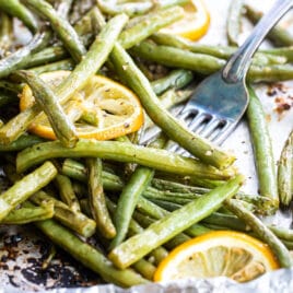 Roasted green beans on a baking sheet with lemon garnish.