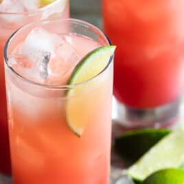 Seabreeze cocktail in three glasses on a silver serving tray with ice and sliced and whole limes.