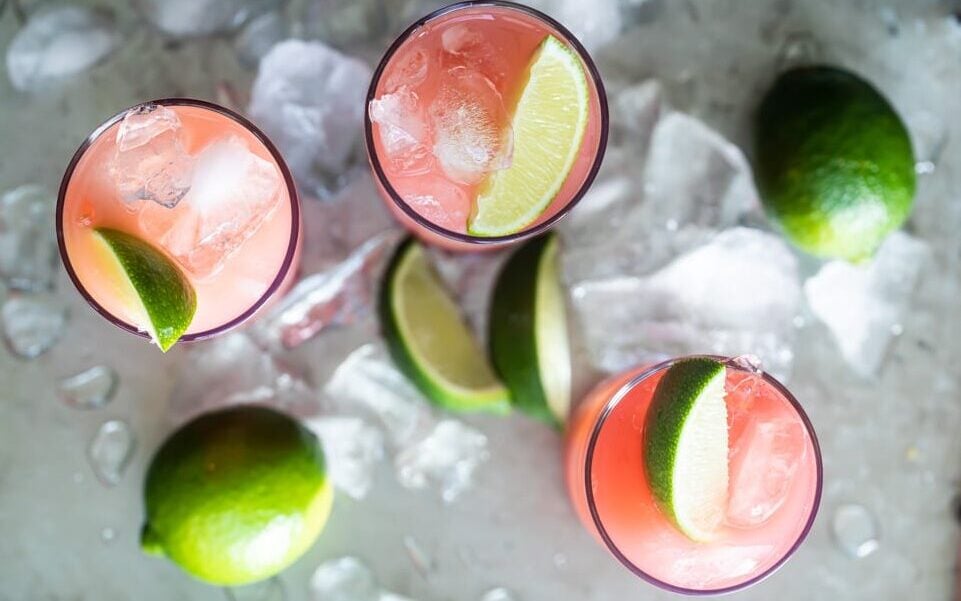 Seabreeze cocktail in three glasses on a silver serving tray with ice and sliced and whole limes.