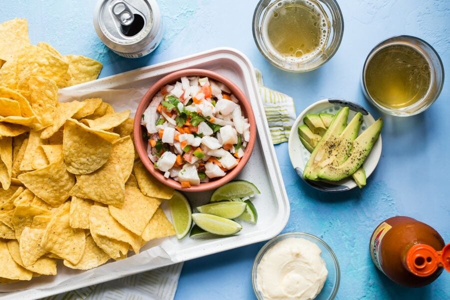 An overhead shot of taliapa ceviche in a pink bowl on a white platter with tortilla chips.
