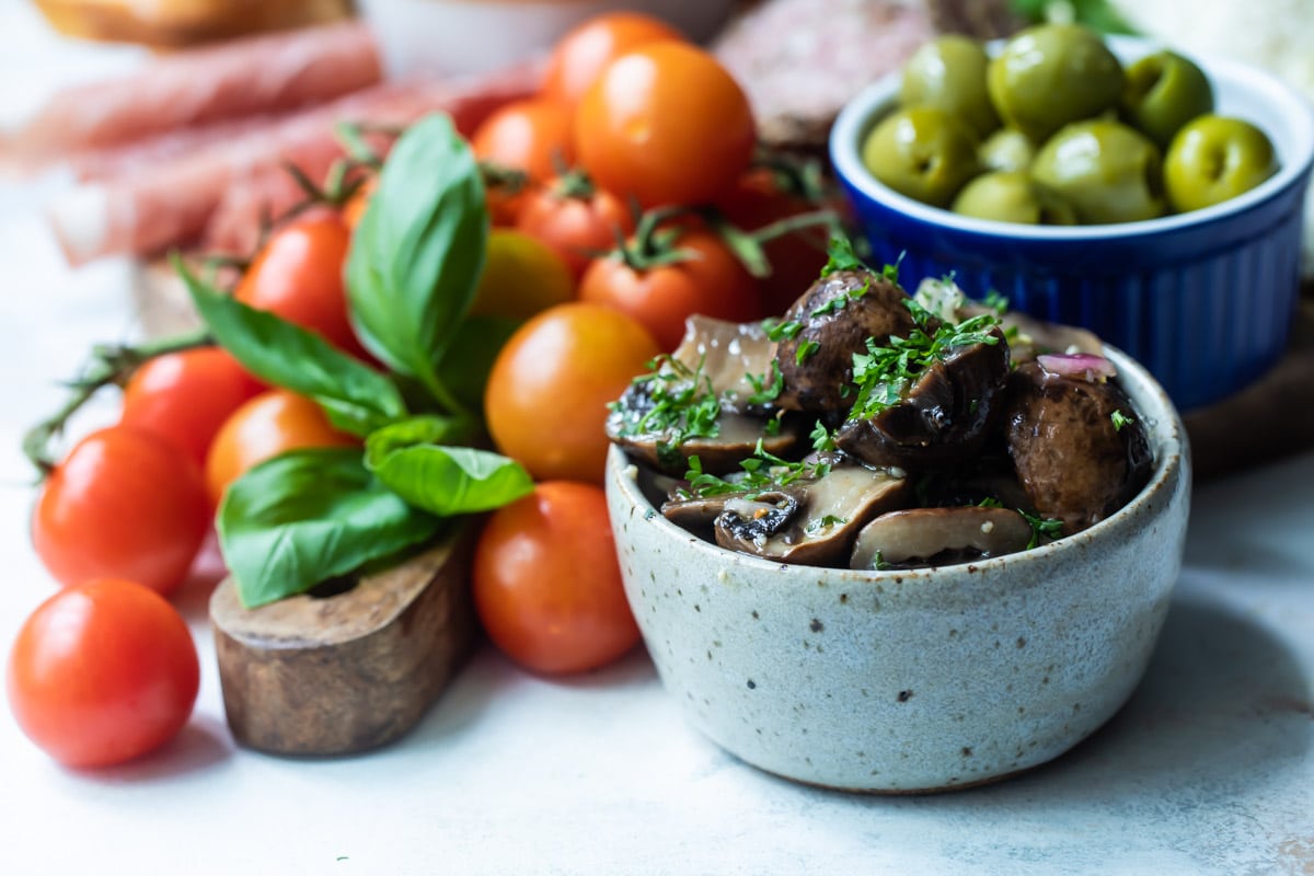 Marinated mushrooms in a gray bowl with vegetables behind them.