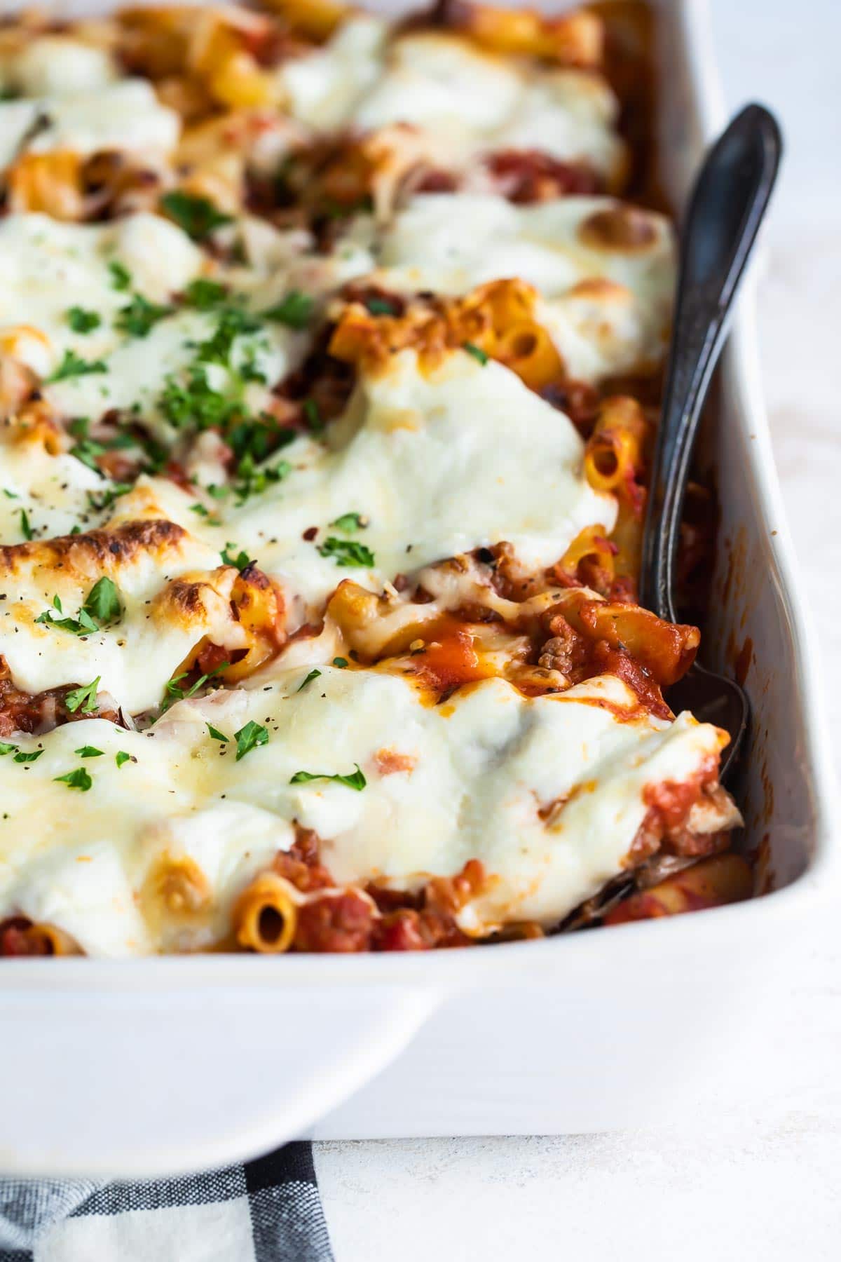 A pan of baked ziti with a spoon in it.