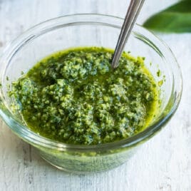 A bowl of pesto with a spoon in it.