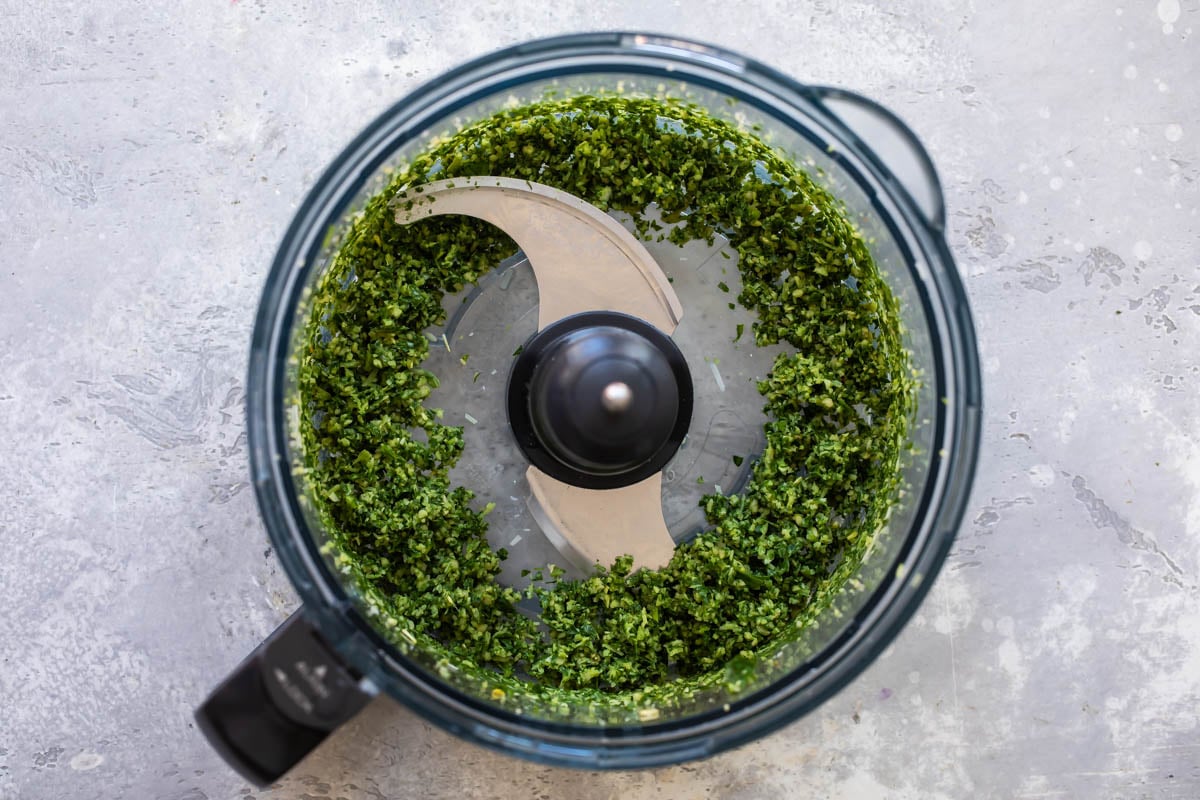 A food processor with basil walnut pesto in it.