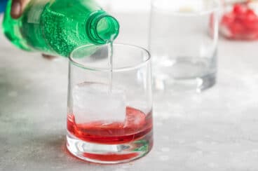 Lemon lime soda being poured over grenadine in a clear glass.