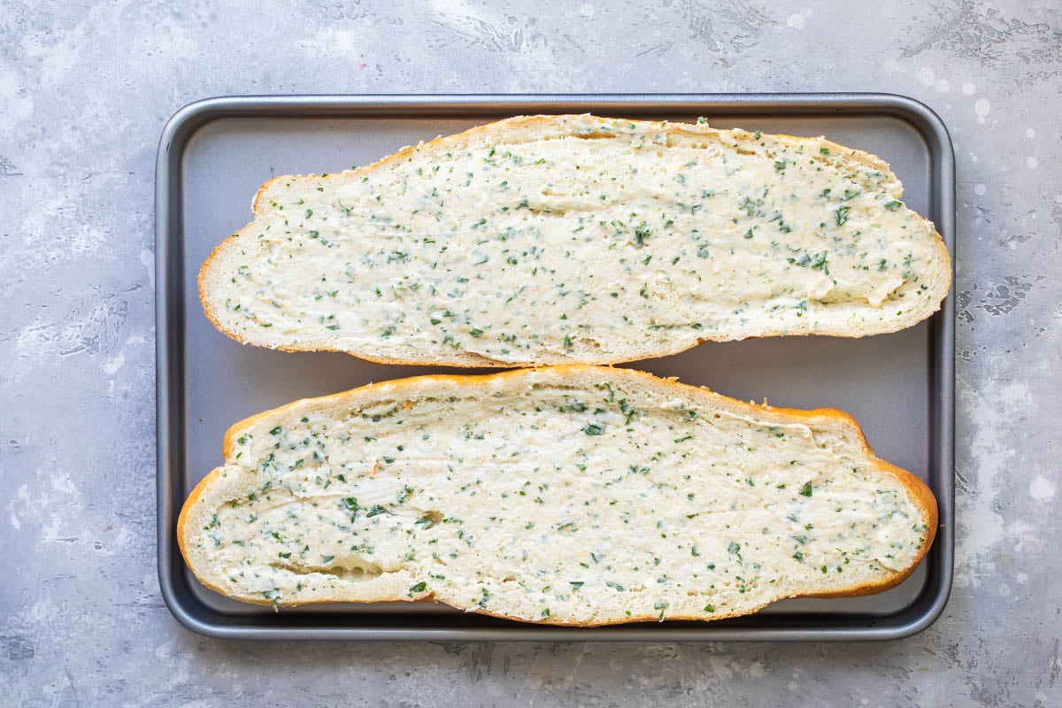An uncooked halved loaf of garlic bread on a baking sheet.
