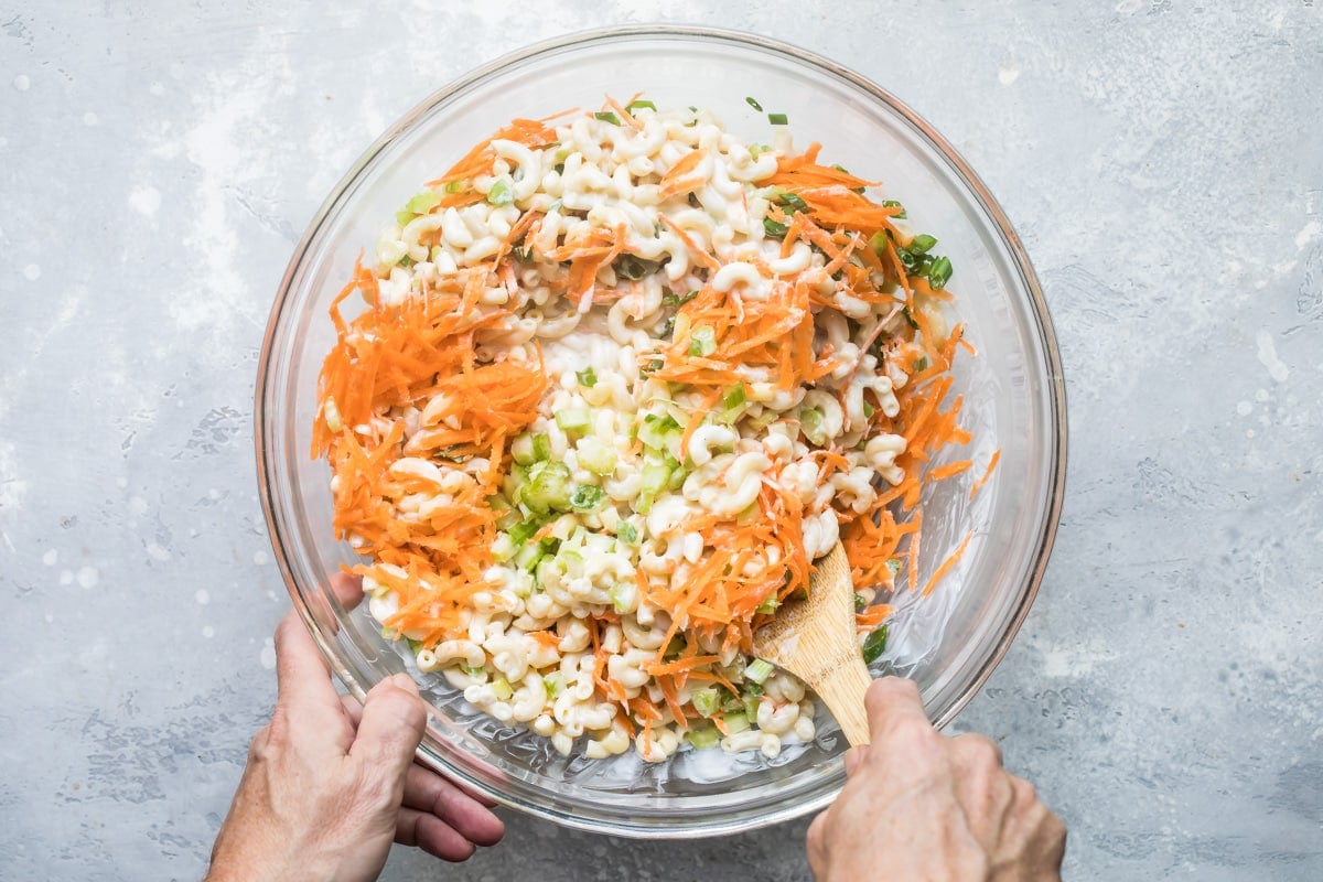 Hawaiian macaroni salad ingredients being mixed together in a clear bowl.