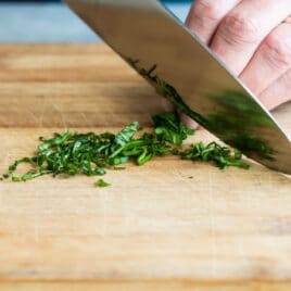 Someone chiffonading basil on a cutting board.