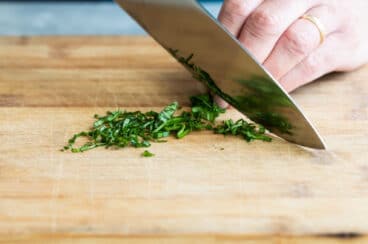 Someone chiffonading basil on a cutting board.