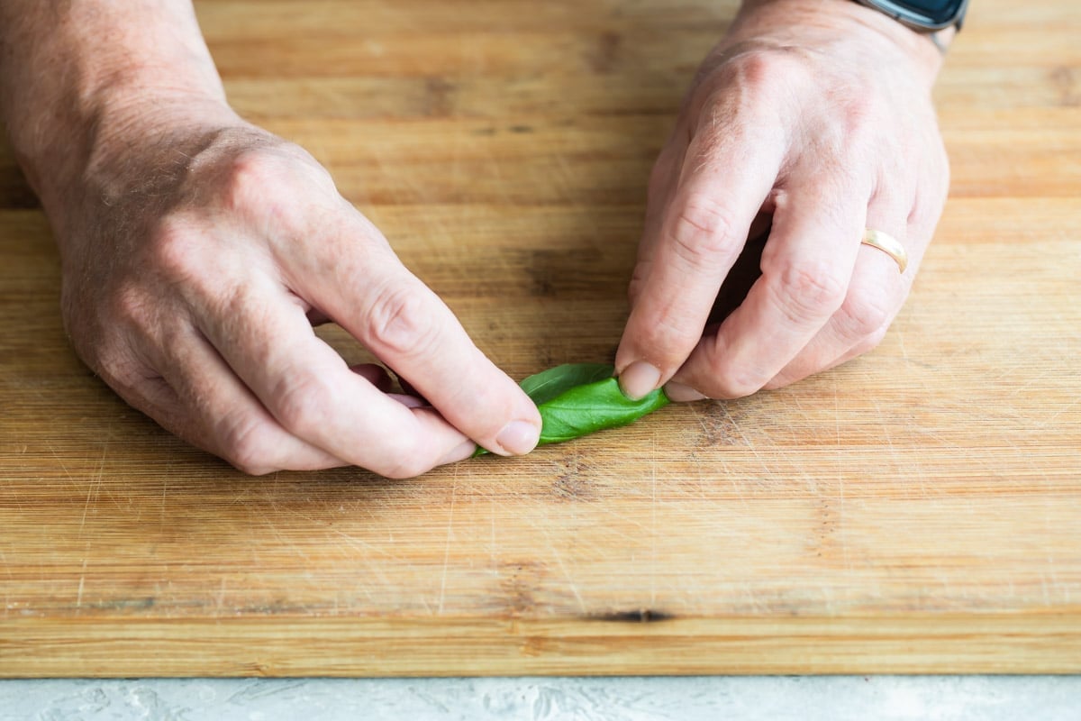 Someone rolling basil on a wooden cutting board.
