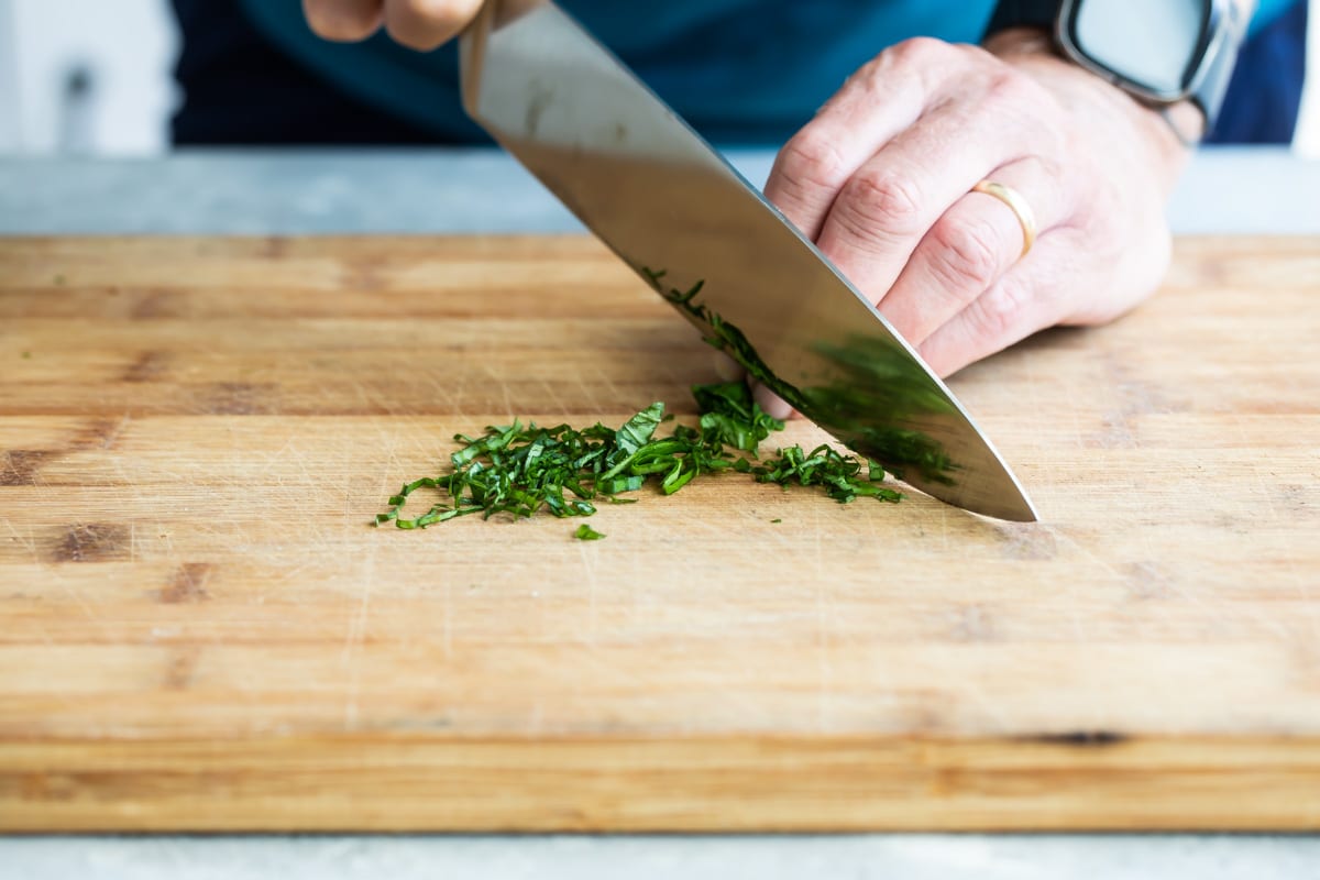 Someone chiffonading basil on a cutting board.