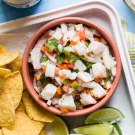 A bowl of tilapia ceviche next to limes and tortilla chips.