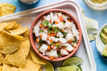 A bowl of tilapia ceviche next to limes and tortilla chips.