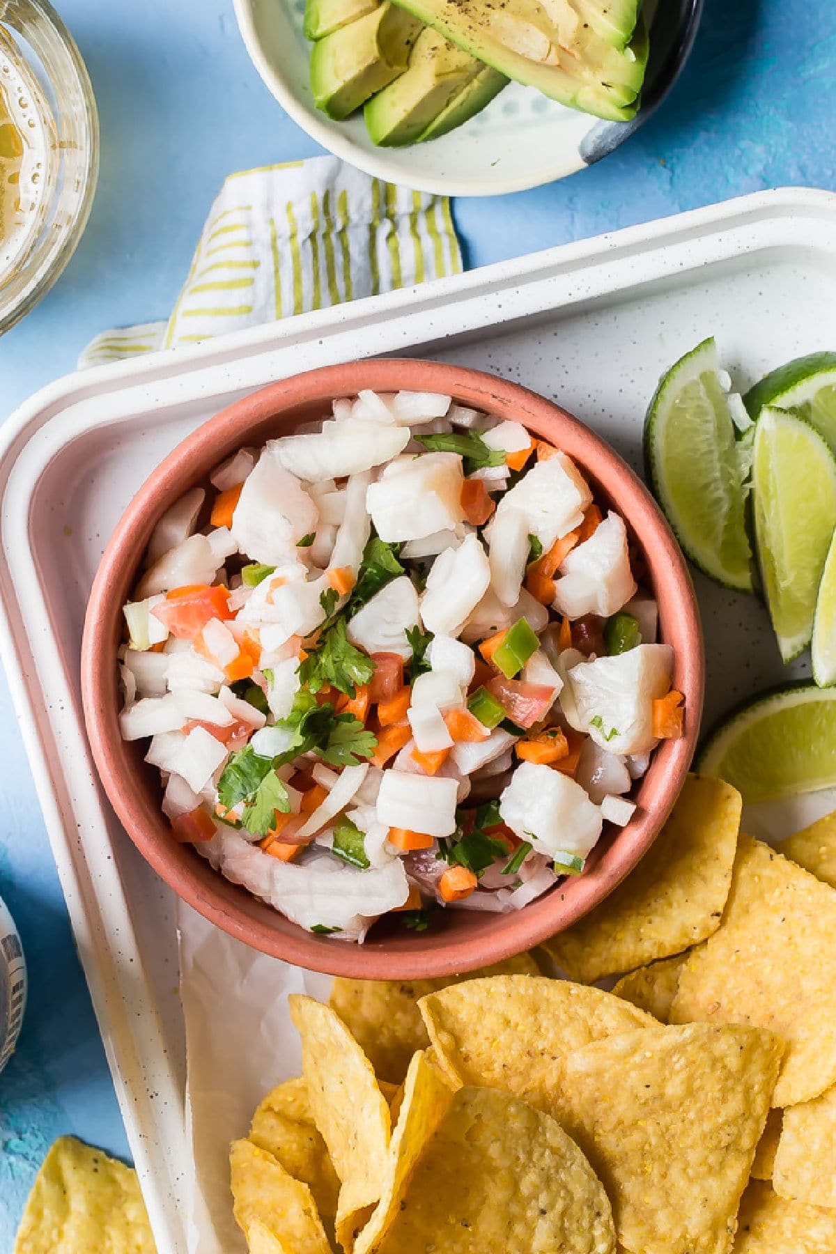 A bowl of tilapia ceviche next to limes and tortilla chips.