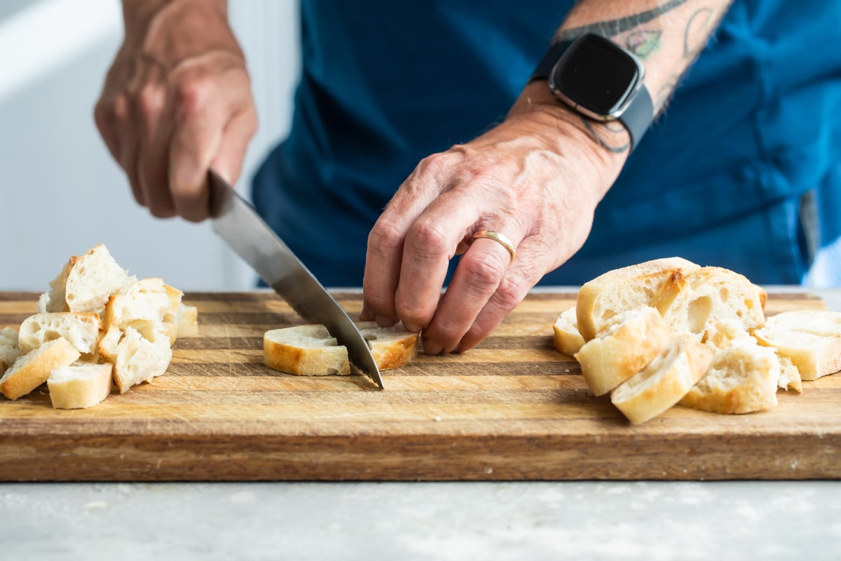 Someone cutting a slice of bread on a wooden cutting board.