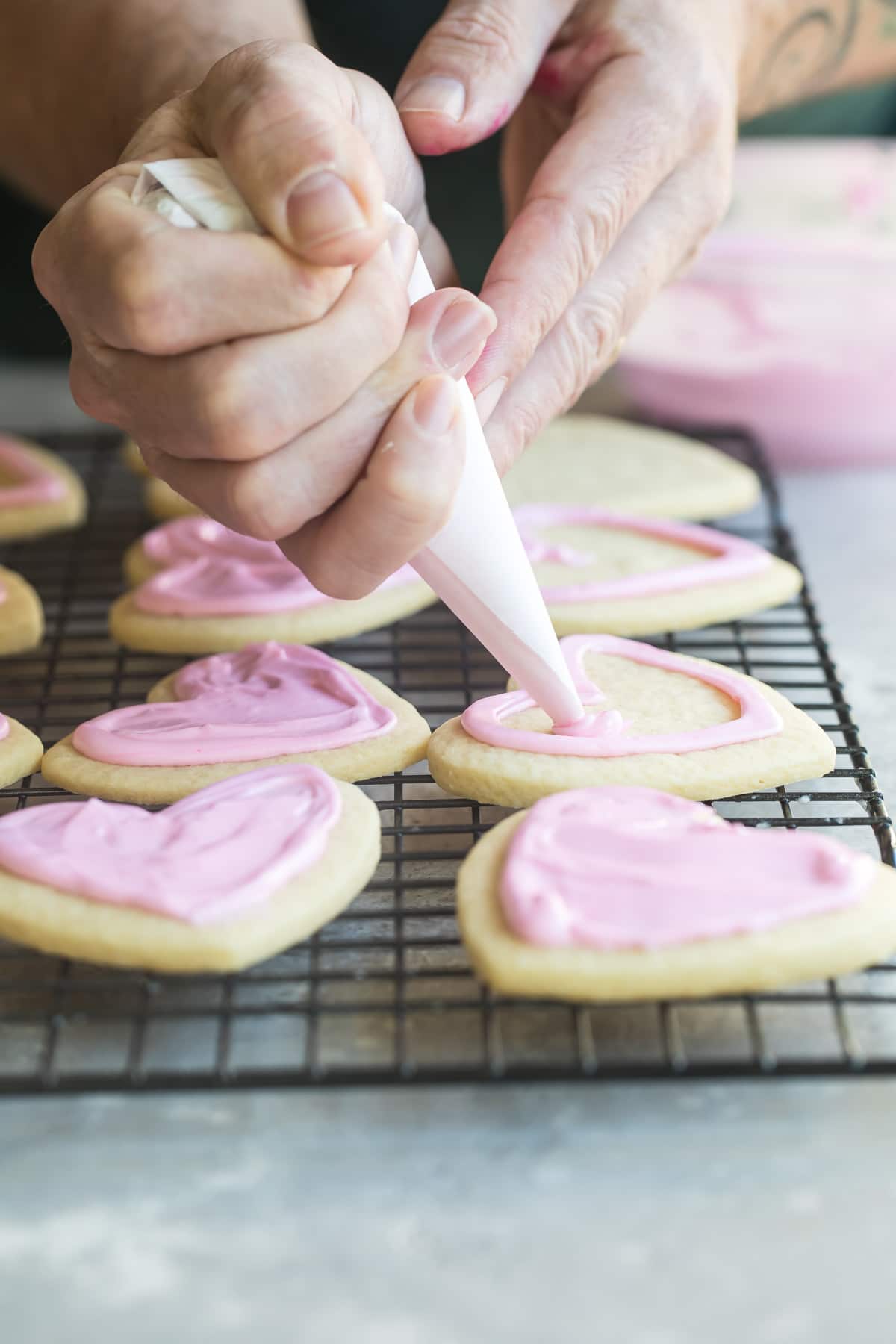 Someone frosting heart sugar cookies with pink royal icing.