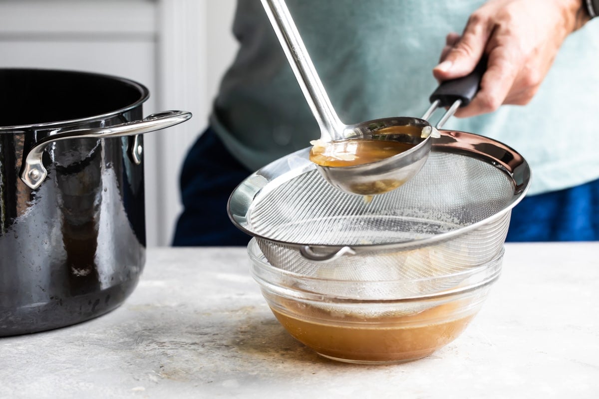 Someone straining brown liquid over a clear bowl.
