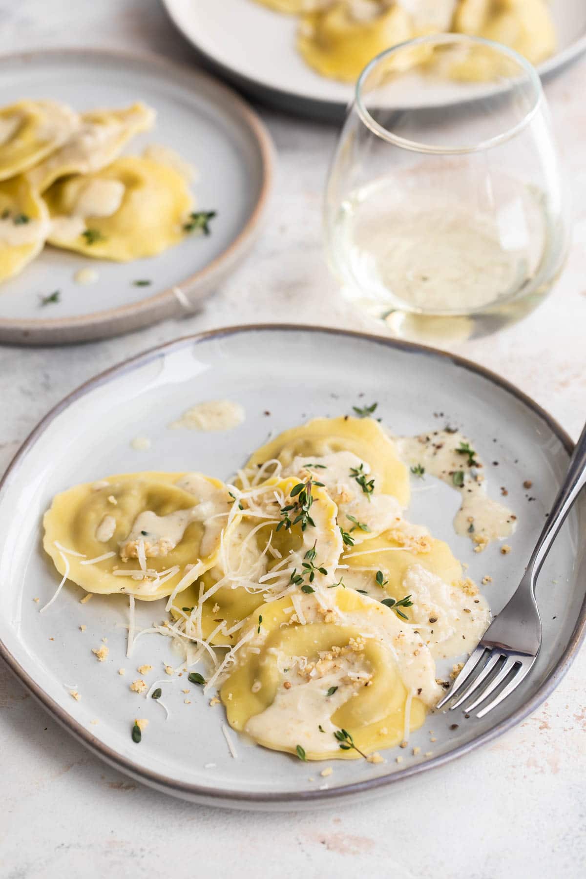 Three plates of mushroom ravioli and a glass of white wine.