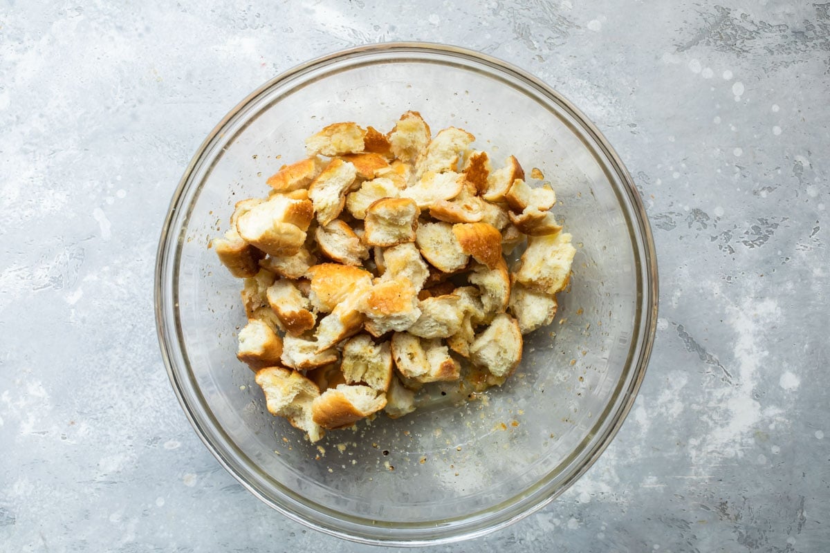 Pieces of bread in a clear bowl with oil and spices.