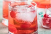 Shirley temples in three clear glasses with a clear bowl filled with cherries.