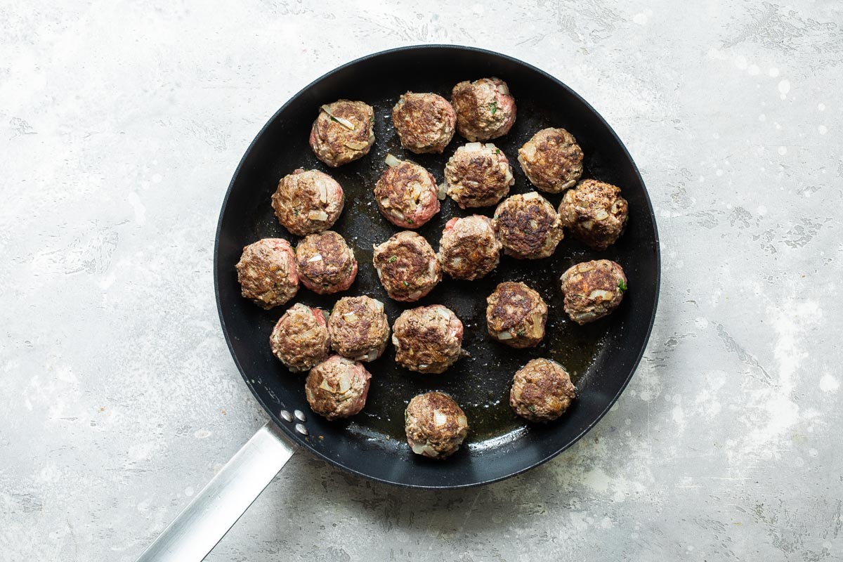 Meatballs being browned in a skillet.