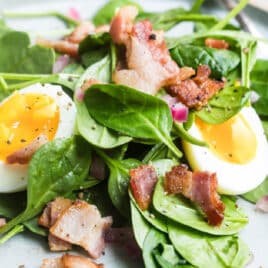 A spinach salad with hot bacon dressing, bacon, and eggs.