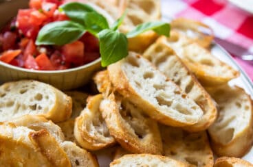 Toasted baguettes on a white platter with bruschetta.