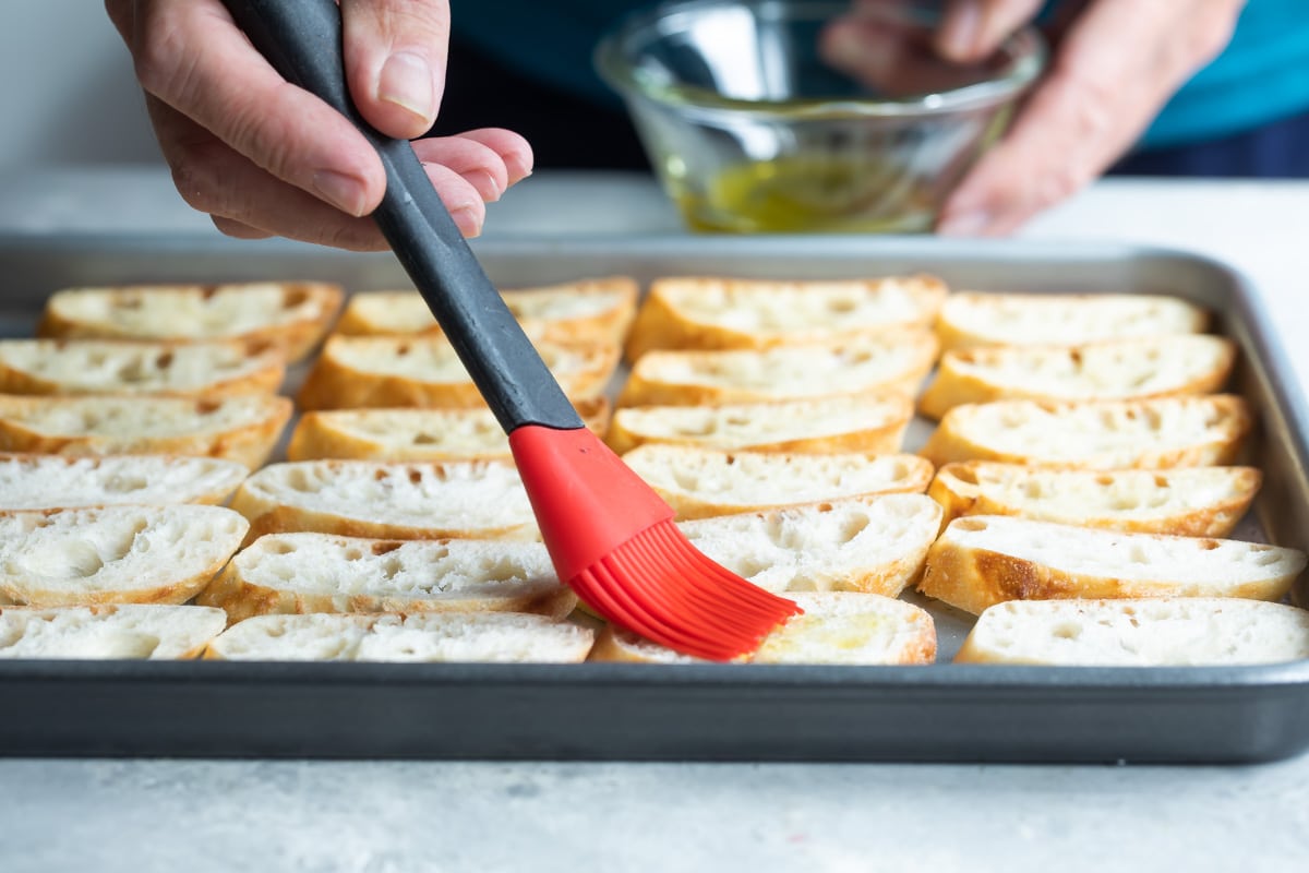 Someone spreading oil onto baguettes.