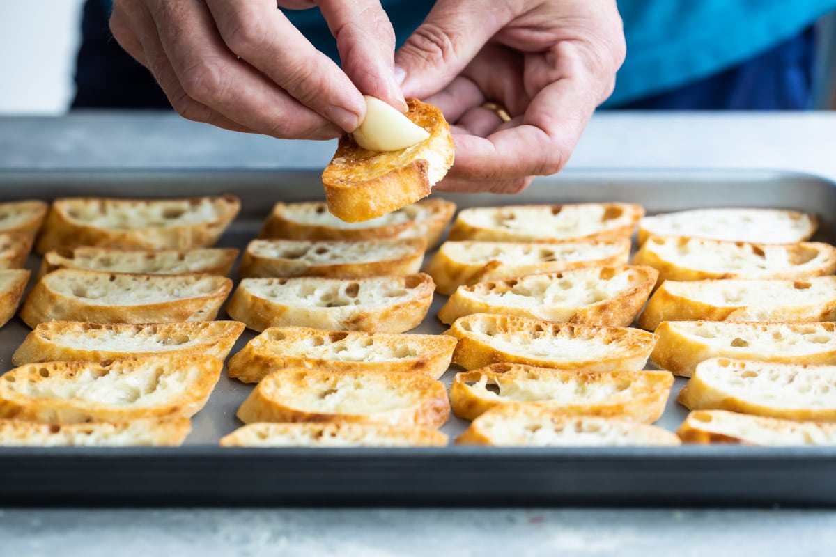 Someone rubbing garlic on a toasted baguette.