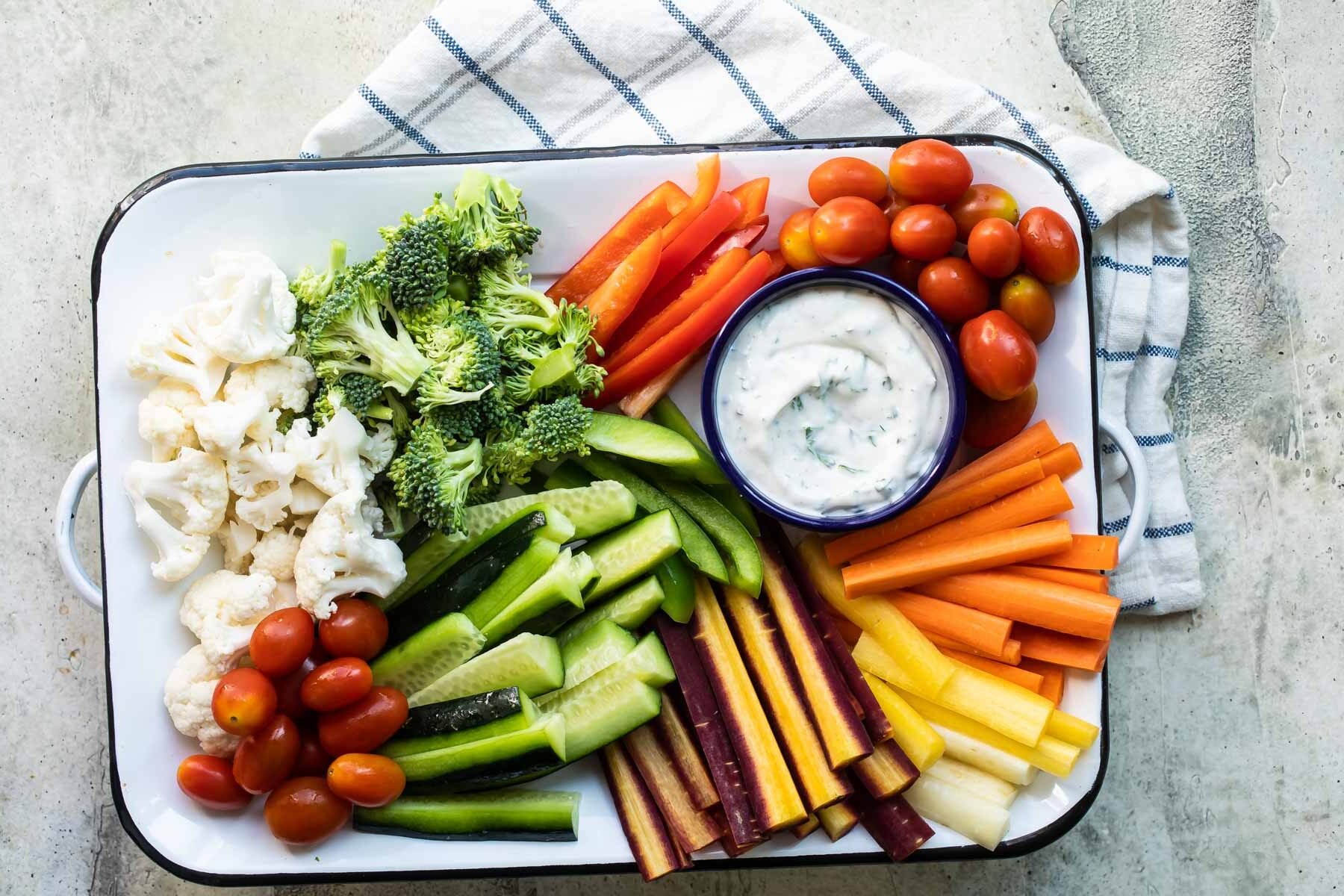 Veggies and veggie dip on a white rectangular platter.