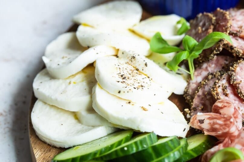 Mozzarella cheese, vegetables and meats on a wooden tray.